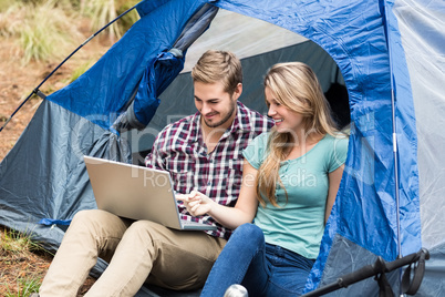 Young pretty hiker couple sitting in a tent looking at laptop