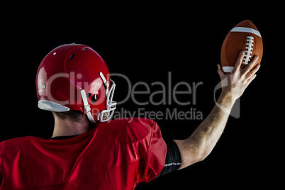Rear view of american football player holding up football