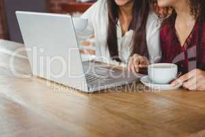 Happy women friends drinking coffee and looking at laptop