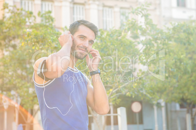 Handsome athlete smiling and putting in headphones