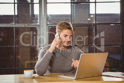 Handsome man phoning and looking at laptop