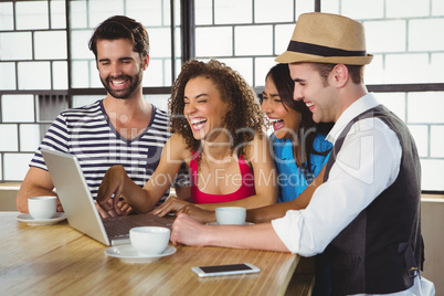 Smiling friends looking at laptop and having coffee