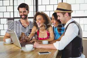 Smiling friends looking at laptop and having coffee