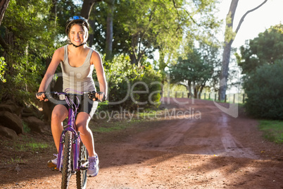 Smiling athletic brunette mountain biking on path