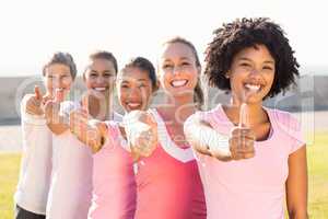 Smiling women wearing pink for breast cancer and doing thumbs up