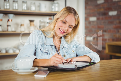 Smiling blonde having coffee and writing in planner
