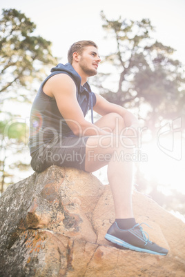 Young happy jogger sitting on rock and looking away