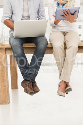Casual designers sitting on wooden desk and using devices