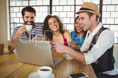 Smiling friends looking at laptop and having coffee