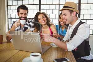 Smiling friends looking at laptop and having coffee