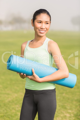 Smiling sporty woman holding exercise mat