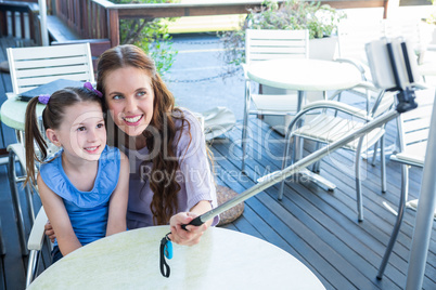 Mother and daughter using selfie stick at cafe terrace