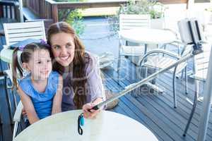 Mother and daughter using selfie stick at cafe terrace