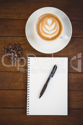 Cup of cappuccino with coffee art and notepad