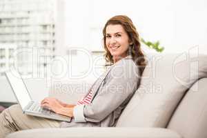 Smiling casual businesswoman sitting on couch with laptop