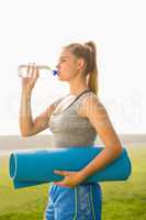 Sporty blonde holding exercise mat and drinking water