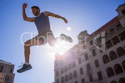 Handsome athlete leaping in front of building