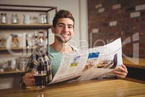 Smiling hipster drinking coffee and reading newspaper