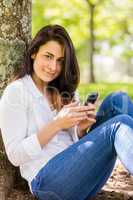 Beautiful brunette sending text in the park