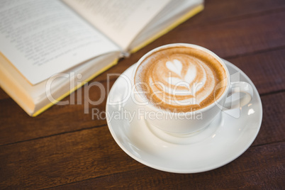 Cup of cappuccino with coffee art next to opened book