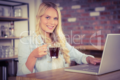 Smiling blonde drinking coffee and using laptop