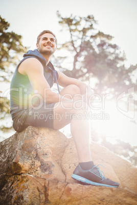 Young happy jogger sitting on rock and looking away