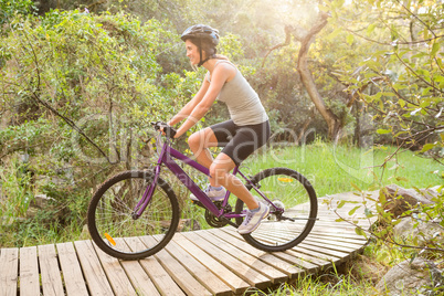 Athletic brunette mountain biking on wooden path