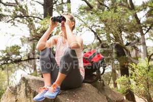 Blonde hiker sitting on rock and  looking through binoculars