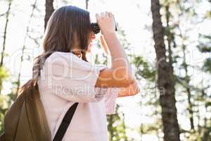 Smiling brunette hiker looking through binoculars