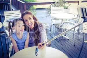 Mother and daughter using selfie stick at cafe terrace