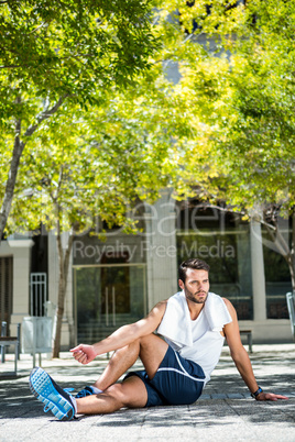 Handsome athlete with towel stretching his leg on the ground