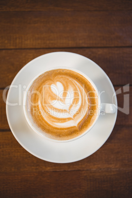 Cup of cappuccino with coffee art on wooden table