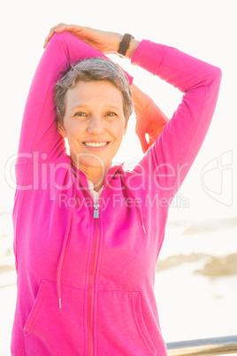 Smiling sporty woman stretching arms at promenade