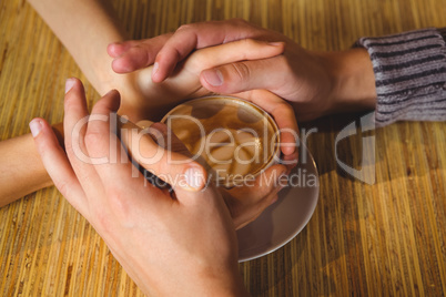 Couple holding hands around cappuccino with coffee art