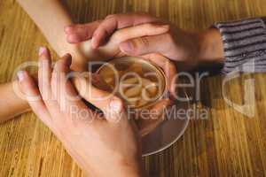 Couple holding hands around cappuccino with coffee art