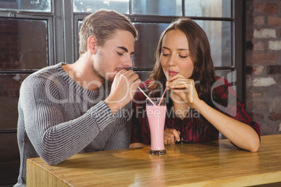 Smiling friends sharing smoothie and drinking through straws