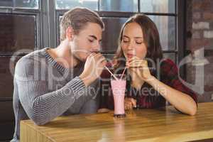 Smiling friends sharing smoothie and drinking through straws