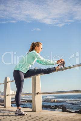 Smiling fit blonde stretching leg on railing