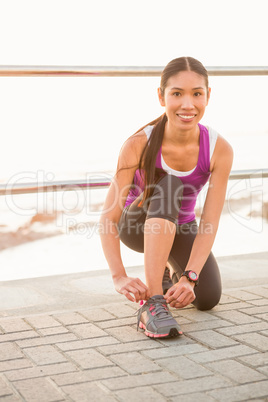 Smiling fit woman tying shoelace at promenade