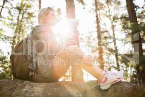 Pretty blonde hiker drinking and sitting on stone