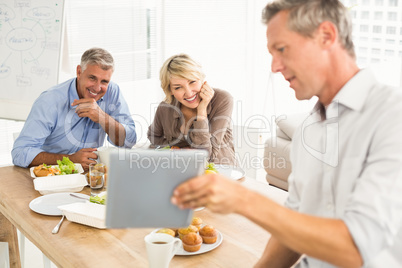Casual business people looking at tablet while lunch