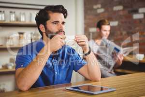 Young man having cup of coffee using tablet