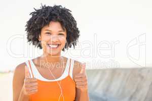 Young sporty woman enjoying music and doing thumbs up