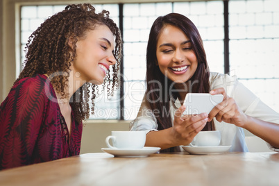 Female friends having coffee and looking at a smartphone