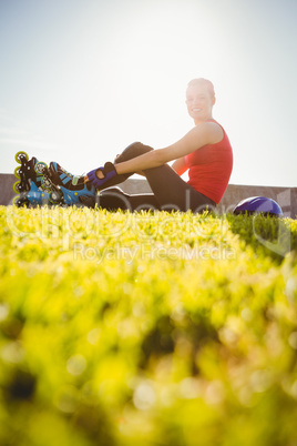 Smiling sporty blonde skater sitting in grass