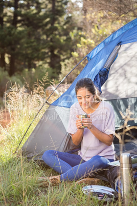 Brunette camper enjoying beverage and sitting in tent