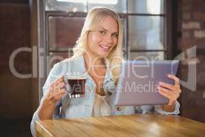 Smiling blonde drinking coffee and holding tablet