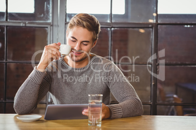 Handsome man drinking coffee and looking at tablet