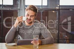 Handsome man drinking coffee and looking at tablet