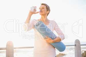 Sporty woman with exercise mat drinking water